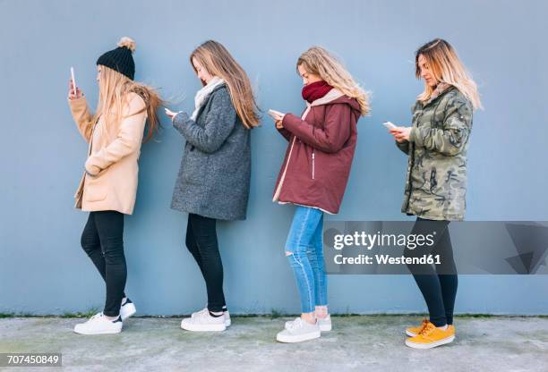 four young women standing in a row using their cell phones - remote location cell phone stock pictures, royalty-free photos & images