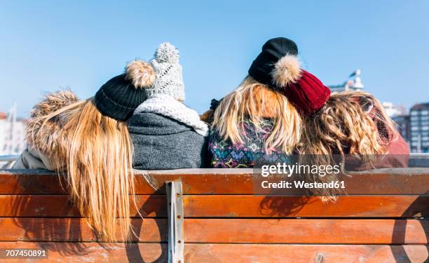 back view of four friends sitting on a bench in winter - ijsmuts stockfoto's en -beelden