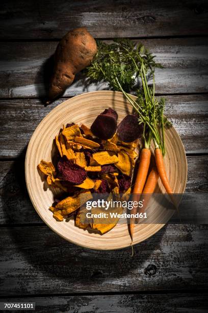 vegetable chips made of carrots, sweet patatoes and beetroot on plate and dark wood - vegetable chips stock pictures, royalty-free photos & images