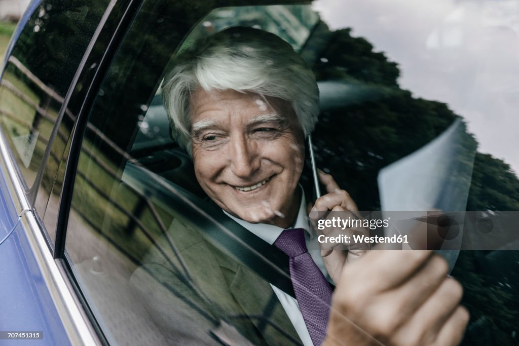 Smiling senior businessman with documents on the phone in a car