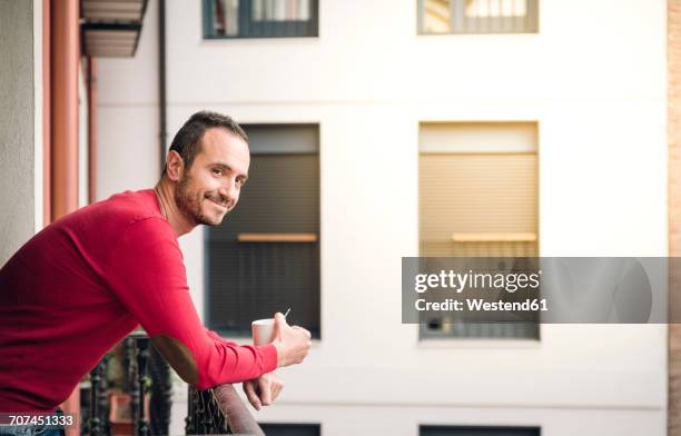 portrait of smiling man standing on balcony with coffee mug - neighbors fotografías e imágenes de stock