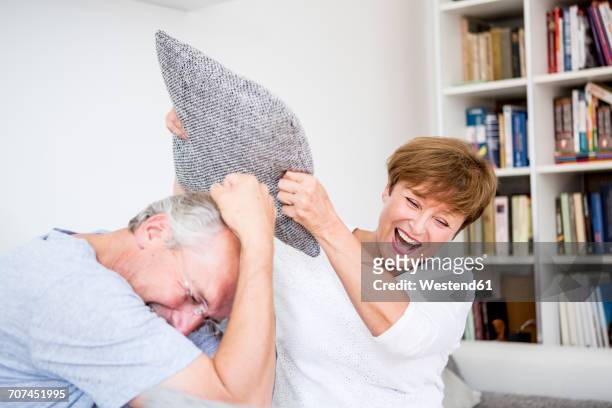 carefree senior couple at home having a pillow fight - naughty wife fotografías e imágenes de stock