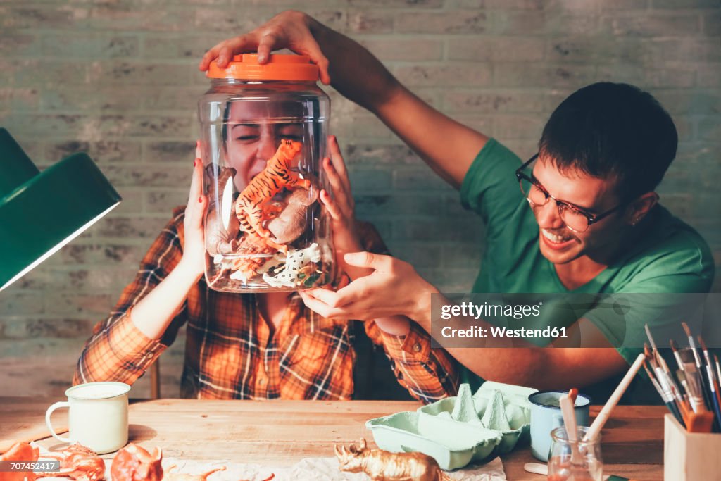 Young couple having fun with animal figurines in jar