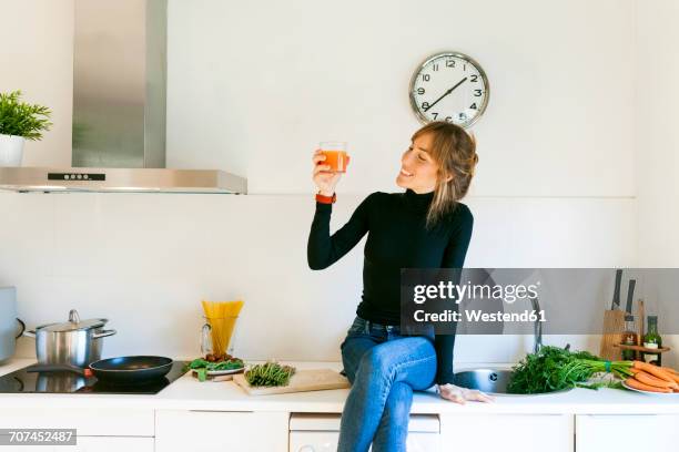 young woman drinking fresh grapefruit juice in her kitchen - junge frau uhr stock-fotos und bilder