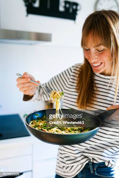 young woman holding pan with vegan pasta dish - young woman cooking in kitchen stock pictures, royalty-free photos & images