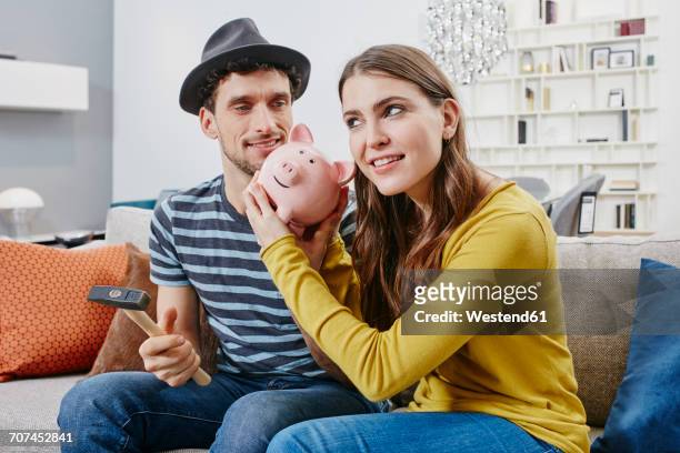 couple in furniture store demolishing piggy bank - couple saving piggy bank stock pictures, royalty-free photos & images