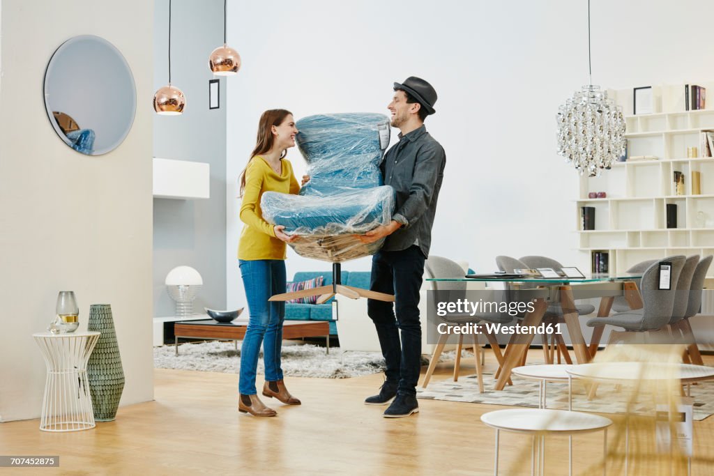 Happy couple carrying new arm chair out of furniture store