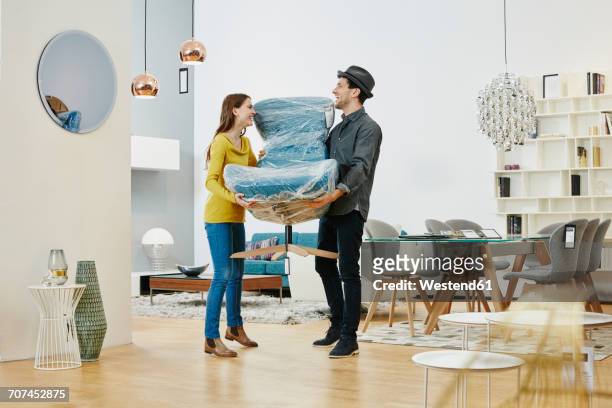 happy couple carrying new arm chair out of furniture store - kaufen stock-fotos und bilder