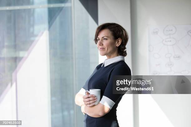 smiling businesswoman with cup of coffee looking out of window - business woman side stockfoto's en -beelden