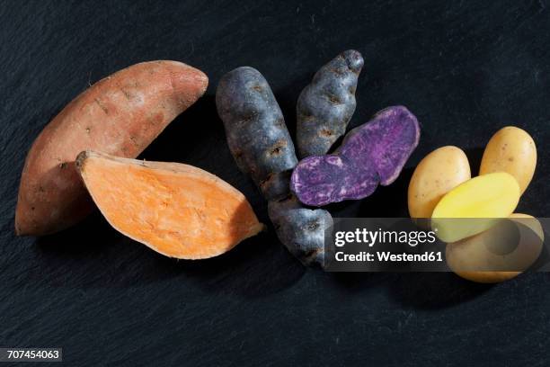 whole and slices sweet potato, purple potato and drillinge on slate - schist stock-fotos und bilder