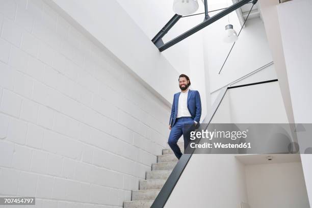 smiling businessman walking down stairs - business stairs stock-fotos und bilder