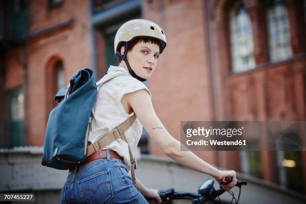 portrait of young woman with cycling helmet and backpack on electric bicycle - cycling helmet photos et images de collection