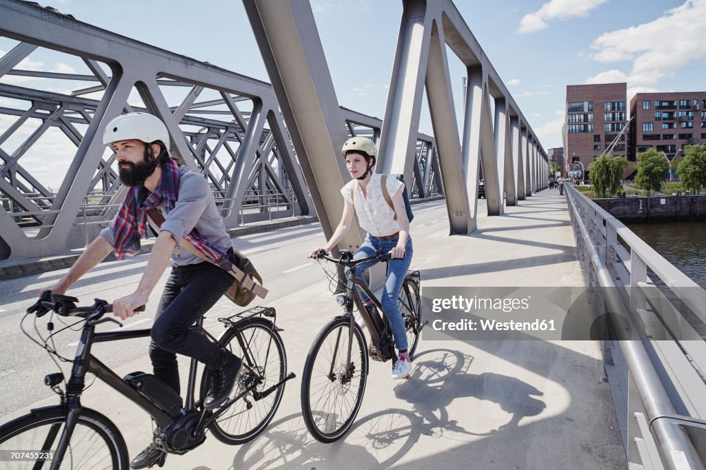 Germany, Hamburg, couple riding electric bicycles on a bridge