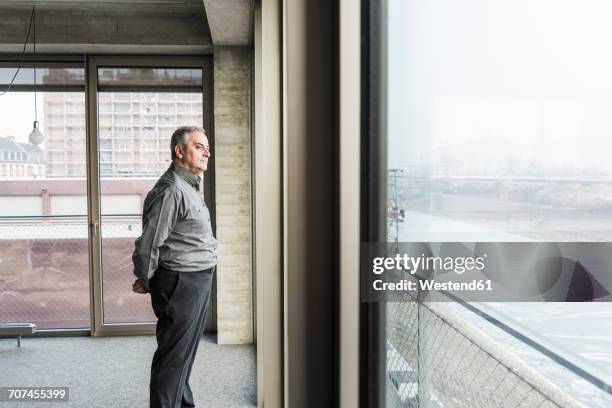 senior businessman looking out of window - hands behind back stockfoto's en -beelden