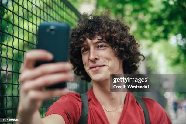 young man taking a selfie with smartphone - curly man stock pictures, royalty-free photos & images