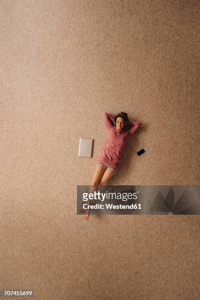 woman lying on carpet wearing headphones, top view - lying down stockfoto's en -beelden