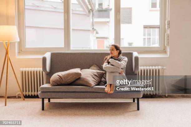 woman sitting on couch looking sideways - froid photos et images de collection