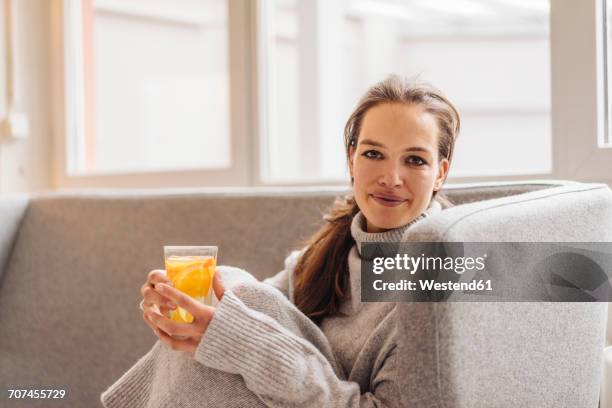 portrait of woman sitting on couch holding fresh drink - jumper stock pictures, royalty-free photos & images