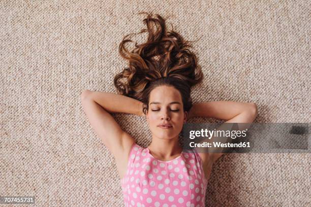 woman lying on carpet with closed eyes - manos detrás de la cabeza fotografías e imágenes de stock
