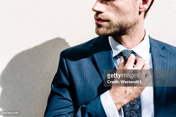 handsome businessman fixing his tie, standing in front of white wall - ties foto e immagini stock