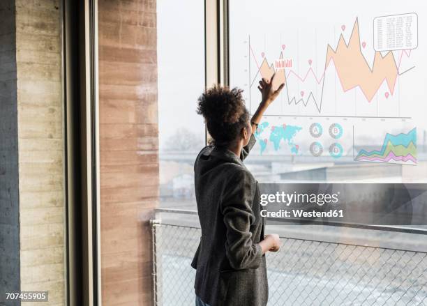 young woman touching windowpane with graph in office - rear view hand window stock pictures, royalty-free photos & images