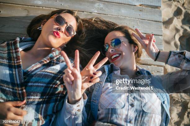 two young women lying on wooden boardwalk showing victory signs - victory sign stock-fotos und bilder