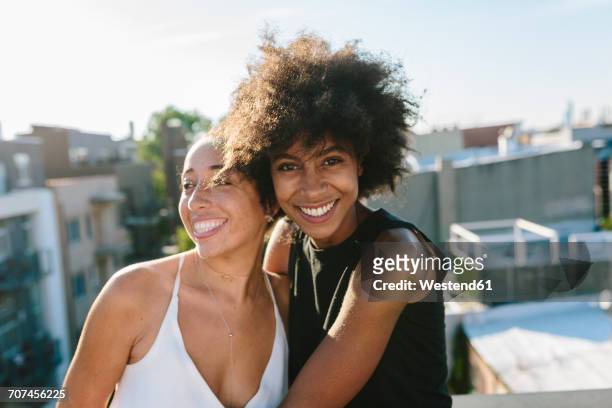 female friends standing on rooftop, embracing - lesbiana fotografías e imágenes de stock