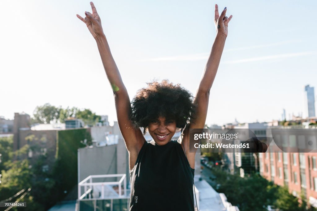 Happy young woman standing on rooftop in Brookly making victory sign