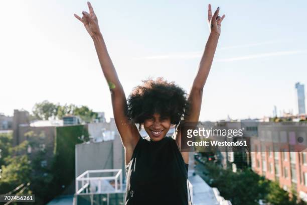 happy young woman standing on rooftop in brookly making victory sign - arms raised stock pictures, royalty-free photos & images