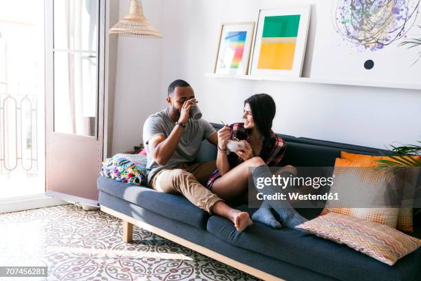 young couple sitting on sofa, eating breakfast - couple couch imagens e fotografias de stock