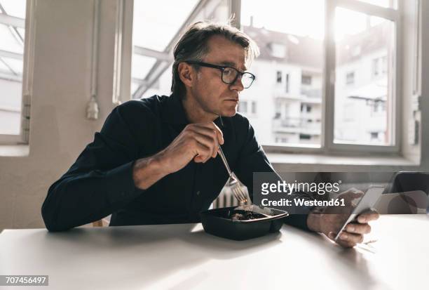 mature businessman checking cell phone during lunch break in office - worker lunch foto e immagini stock