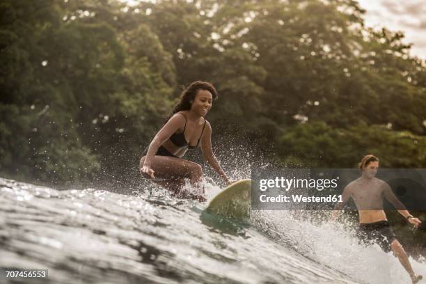 indonesia, java, happy woman and man surfing - indonesia surfing imagens e fotografias de stock