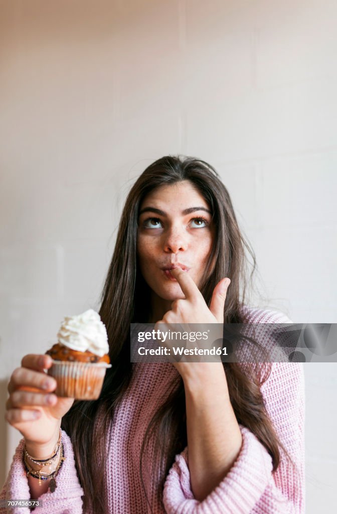 Young woman eating a cup cake with whipped cream, licking finger