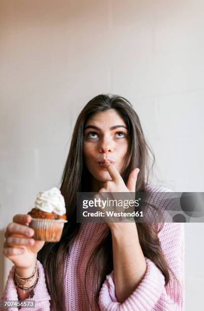 young woman eating a cup cake with whipped cream, licking finger - cupcake stock-fotos und bilder