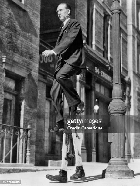 1930s INVENTOR WALTER NILSSON SITTING ON UNICYCLE WHILE WALKING TO WORK ON STILTS LOS ANGELES USA