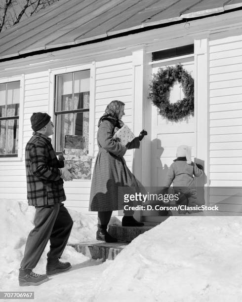 1950s 1960s VISITING FAMILY OF THREE AT FRONT DOOR CARRYING CHRISTMAS GIFTS