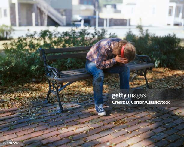 1960s 1970s 1980s TROUBLED TEENAGE BOY WITH LONG HAIR AND HEADBAND SITTING ON CITY PARK BENCH HOLDING FACE IN HANDS