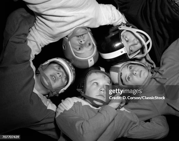 1960s FIVE BOYS IN HUDDLE WEARING HELMETS & FOOTBALL JERSEYS THE VIEW IS FROM INSIDE THE HUDDLE LOOKING UP