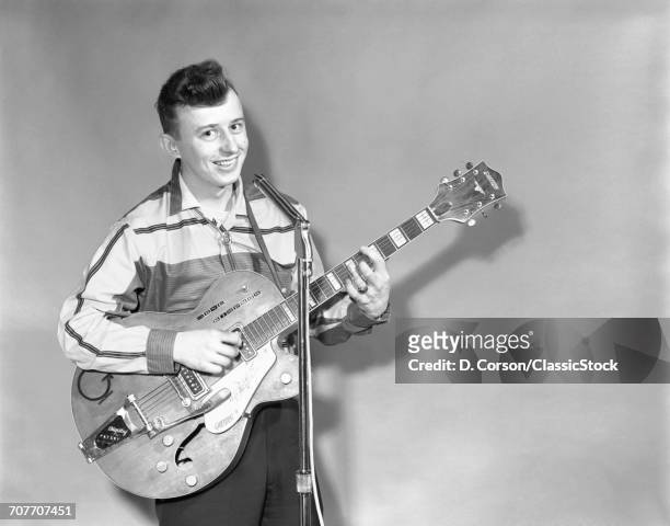 1950s TEENAGE BOY SINGING PLAYING GUITAR INTO MICROPHONE LOOKING AT CAMERA