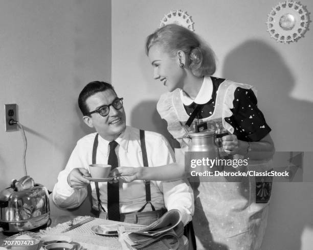 1950s COUPLE AT BREAKFAST TABLE MAN READING NEWSPAPER SMILING AT WIFE HOLDING COFFEE CUP AND PERCOLATOR POT