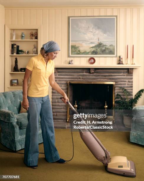 1960s WOMAN WEARING HEAD SCARF BELL BOTTOM PANTS CLEANING LIVING ROOM WITH UPRIGHT VACUUM CLEANER