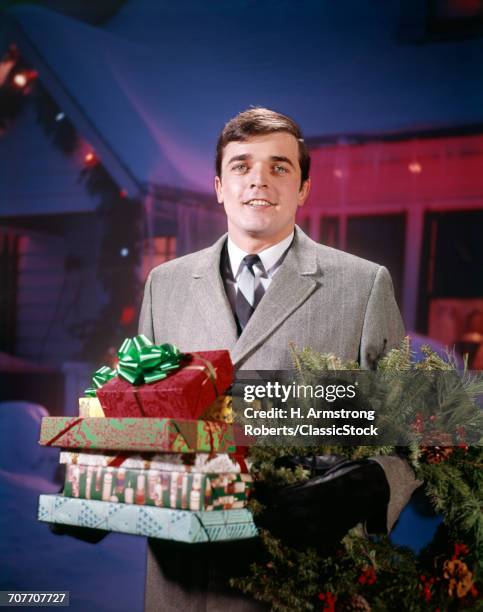 1960s 1970s SMILING MAN HOLDING WRAPPED GIFT PRESENTS AND A PINE BOUGH WREATH LOOKING AT CAMERA