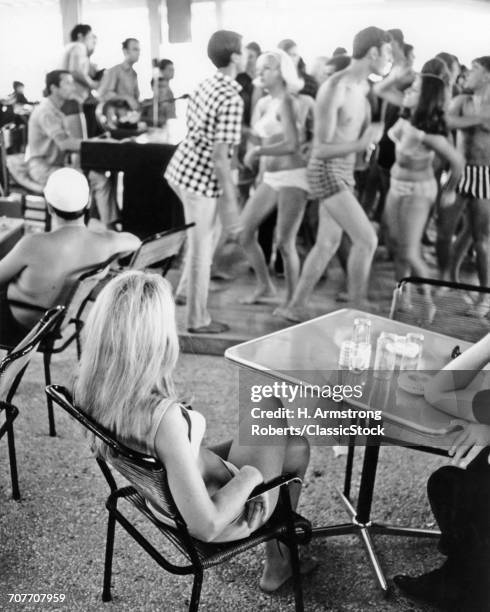 1960s LONG BLONDE HAIR WOMAN SITTING WATCHING GROUP OF YOUNG SPRING BREAK TEENS DANCING WEARING BEACH BATHING SUITS SEASIDE