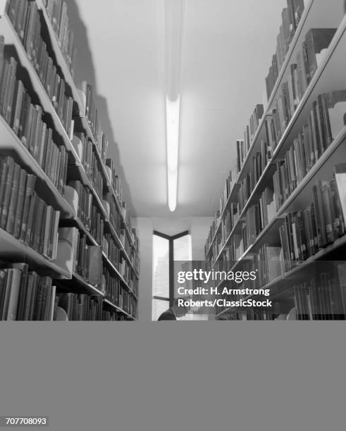 1960s YOUNG MAN STUDENT READING STUDYING AMONG LIBRARY BOOK STACKS