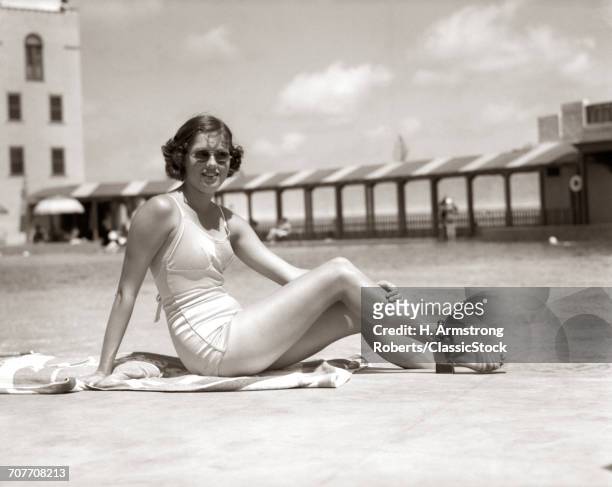 1930s WOMAN SITTING POOL SIDE LOOKING AT CAMERA WEARING FASHIONABLE SUNGLASSES BATHING SUIT AND SANDALS MIAMI BEACH FLORIDA USA