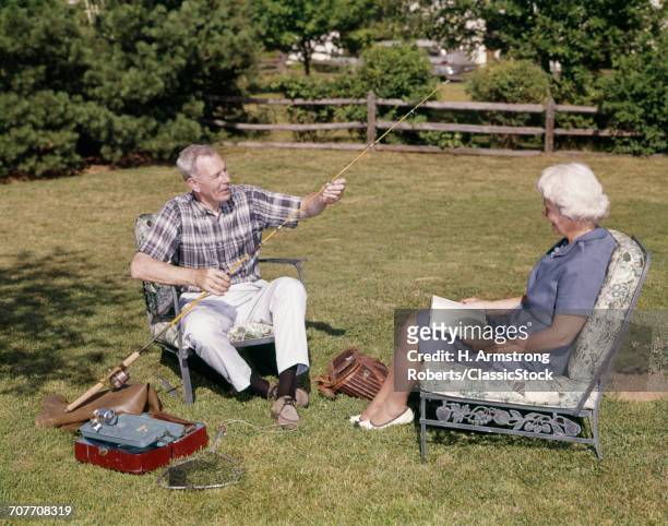 1960s OLDER COUPLE SITTING IN YARD WOMAN READING MAN WORKING WITH FISHING TACKLE GEAR