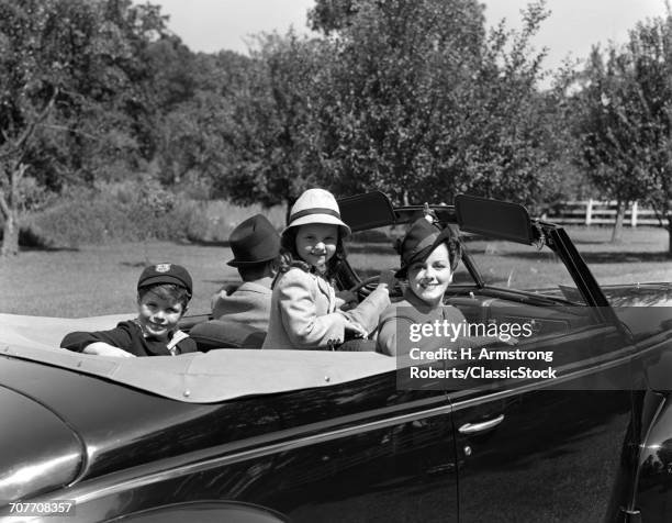 1930s 1940s FAMILY OF 4 IN CONVERTIBLE CAR FATHER DRIVING MOTHER DAUGHTER SON ARE TURNED LOOKING AT CAMERA SMILING