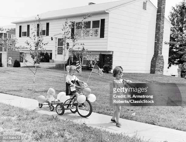 1960s GIRL WITH BUGLE LEADING SISTER ON TRICYCLE DECORATED WITH BALLOONS AMERICAN FLAGS FOR JULY 4TH HOLIDAY SIDEWALK PARADE