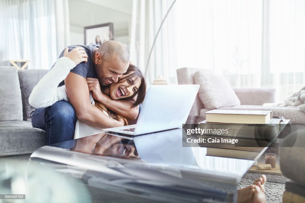 Playful couple hugging and using laptop in living room