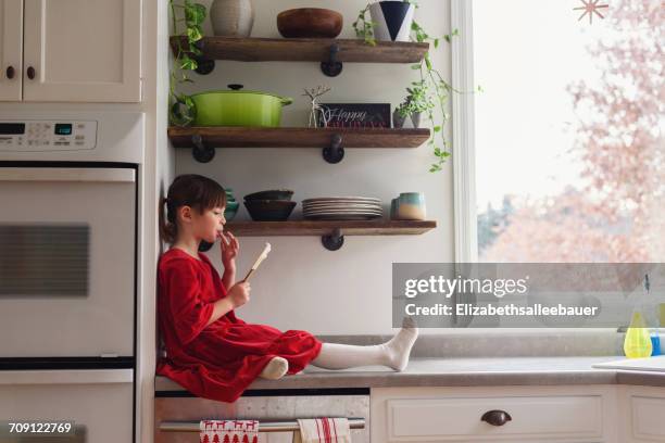 girl sitting on kitchen counter with a spatula eating frosting - girls licking girls stockfoto's en -beelden